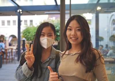 two people smiling,looking at the camera and holding thumbs up, one is wearing a mask