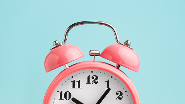 Photo of top half of a pink alarm clock in front of a light blue background.