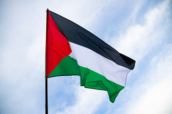 Photo of the Palestinian flag flying in front of a partly clouded blue sky