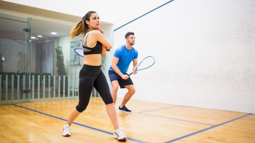Photo of 2 people holding rackets on a squash court focusing instensely